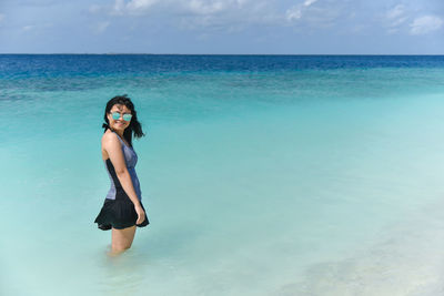 Portrait of young woman standing in sea against sky