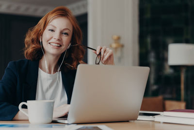 Portrait of smiling woman using laptop on desk in office