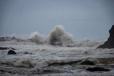 Waves splashing on rocks at shore against sky