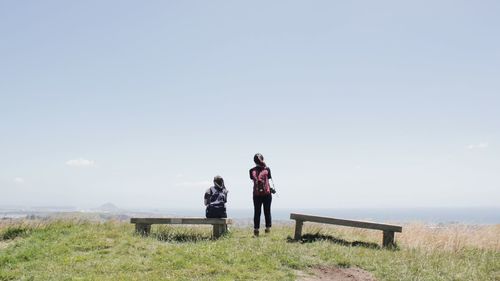 Rear view of people sitting on land against sky