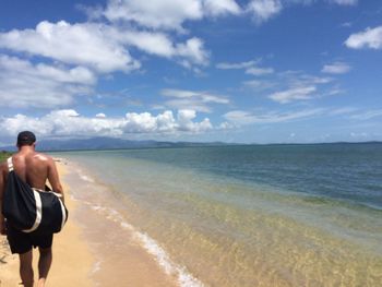 Rear view of shirtless man on beach against sky