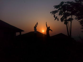 Silhouette people by tree against sky during sunset