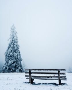 Snow covered bench against clear sky during winter