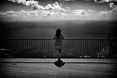 Rear view of woman standing by railing against sea