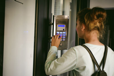 Side view of young woman using intercom