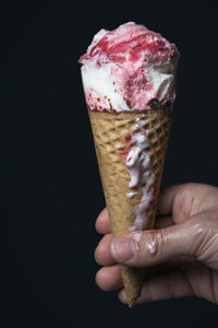 Person holding ice cream cone against black background