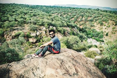 Young woman sitting on rock against mountain