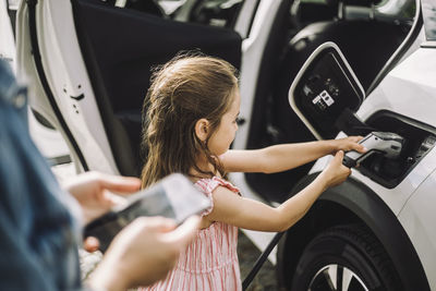 Daughter plugging cable while charging electric car