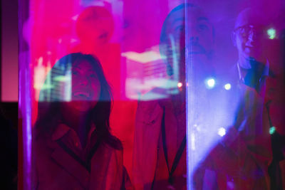Happy male and female business colleagues seen through glass at illuminated exhibition center