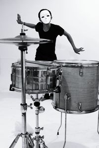 Man wearing mask standing by drum kit against white background