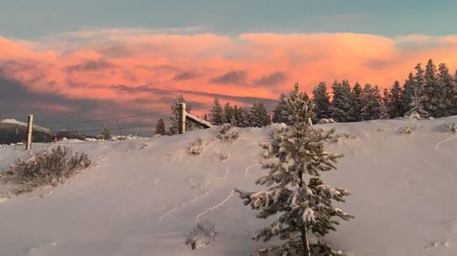 Snow covered landscape against sky during sunset