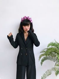 Portrait of young woman wearing black suits standing against plants over white background 