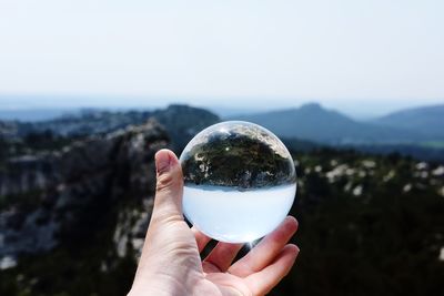 Cropped image of hand holding crystal ball against mountains