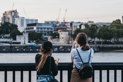 Rear view of woman on railing by river against sky in city