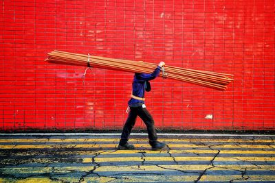 Side view of man carrying metallic rods while walking against wall
