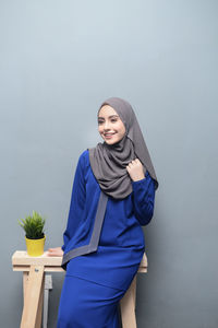 Smiling young woman wearing hijab against gray wall