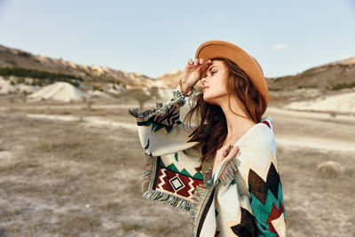 Side view of woman wearing hat while standing against sky