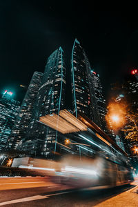 Illuminated buildings by street against sky at night