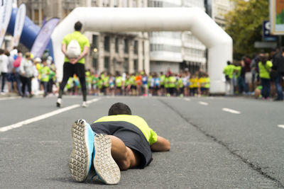 Full length of man lying down with runners in background during competition on road