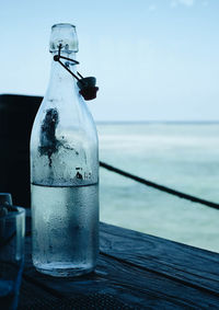 Close-up of glass bottle on table by sea against sky