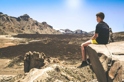 Rear view of man sitting on rock