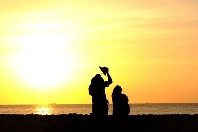 Silhouette friends at beach against sky during sunset