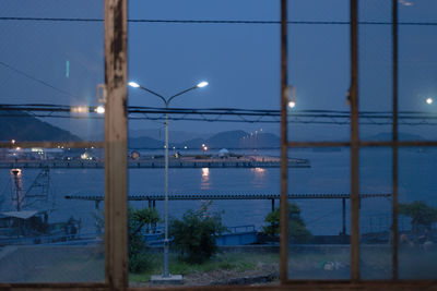 Illuminated street lights by sea against sky at dusk