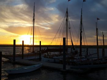 Sailboats moored at harbor against sky during sunset