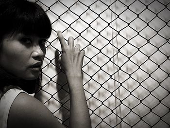 Portrait of young woman standing by chainlink fence