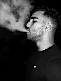 Close-up side view of young man smoking against black background