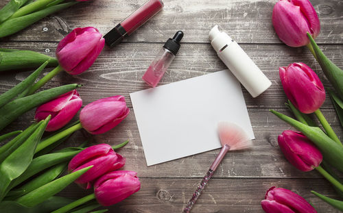  workspace with cosmetics, lipstick and tulip flowers on wooden background. flat lay, top view