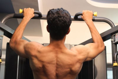 Rear view of shirtless young man exercising in gym