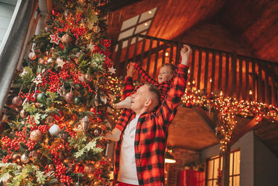 Candid authentic happy dad and son in red plaid pajamas fooling around at wood lodge xmas decorated