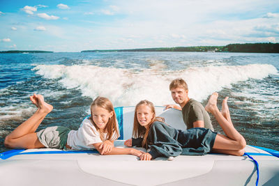 Full length of smiling father and daughter relaxing on boat in sea against sky