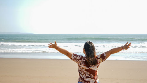 Rear view of woman standing at beach against clear sky