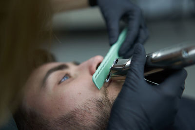 Portrait of young man who sitting in barbershop and woman hairdresser cut hair