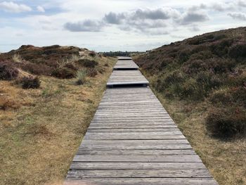 Boardwalk leading towards landscape against sky