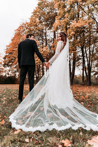 Newlywed couple standing against trees during autumn