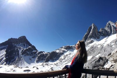 Woman photographing on snow covered mountains against clear sky