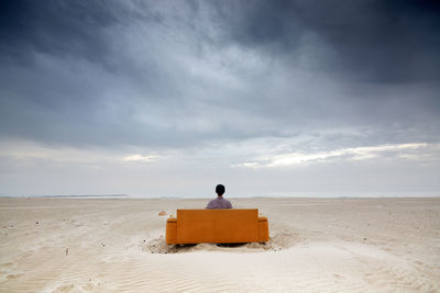 A man siting on a sofa at the beach during a stormy day