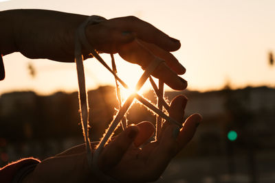 Close-up of hand holding orange rope sky during sunset