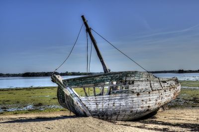 Abandoned boat moored on beach against sky