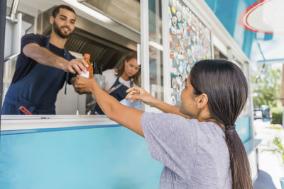 Confident young male owner standing in food truck giving bottle to female colleague