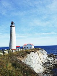 Lighthouse on beach by sea against sky