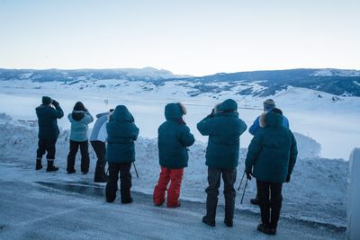 Rear view of people wearing warm clothing standing on snow covered landscape