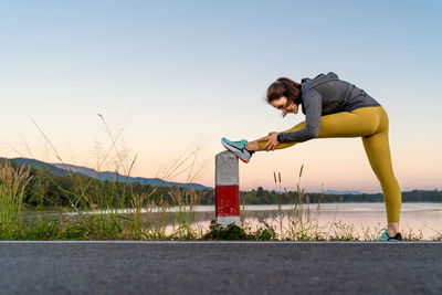 Side view of a woman stretching her arms and legs before her morning exercise at local lake park