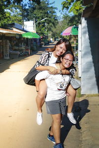 Full length portrait of smiling teenage girl giving piggyback to sister on road