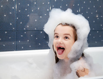 Smiling girl playing with soap sud in bathtub