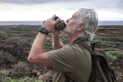 Side view of senior man drinking water while standing on field