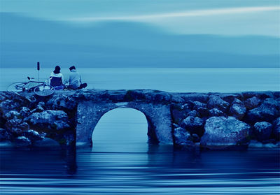 People on rocks by sea against sky